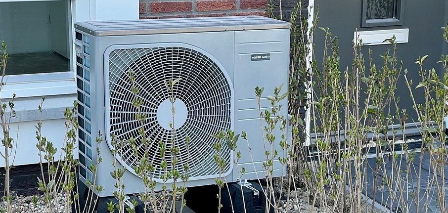 Eine Wärmepumpe ist auf einem weißen Schotterbett vor einer Haustür aufgebaut.