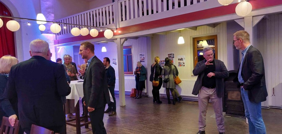 Menschen stehen in Grüppchen in einem Saal und sprechen miteinander