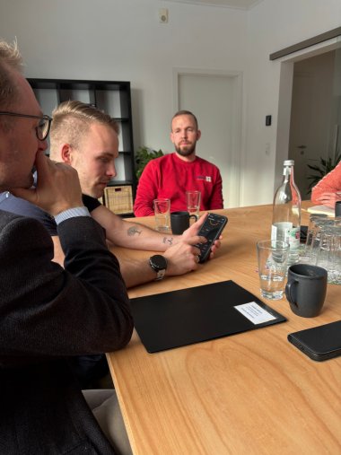 Malte Narz (zweiter von links) erläutert die Steuerung einer modernen Wärme- und Stromversorgung per App. Sie schauen gemeinsam auf ein Smartphone