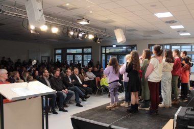 Auch der Schulchor der OWS singt zur Eröffnung. Etwa 30 Kinder sind von schräg hinten zu sehen. Sie stehen auf einer kleinen Bühne und singen vor Publikum