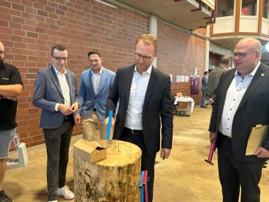 Landrat DR. Mischak auf der Ausbildungsmesse: Er schlägt mit einem Hammer einen Nagel in ein Holzklotz