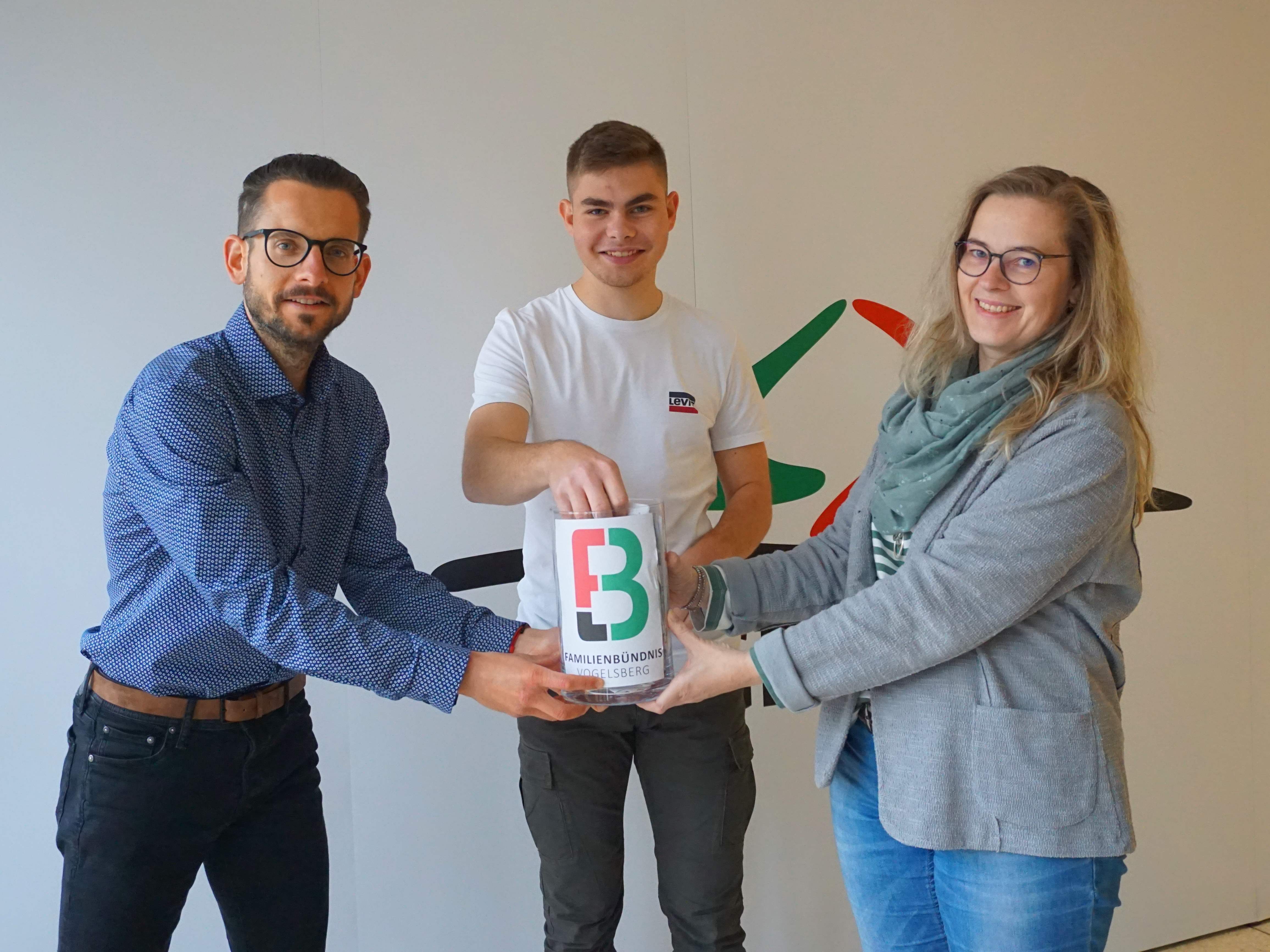 Auszubildender Finn Hildebrand (Mitte), Simon Päbler, Sprecher des Familienbündnisses, und Sandra Obenhack vom Familienbündnis bei der Ziehung für den 100-Euro-Einkaufsgutschein.