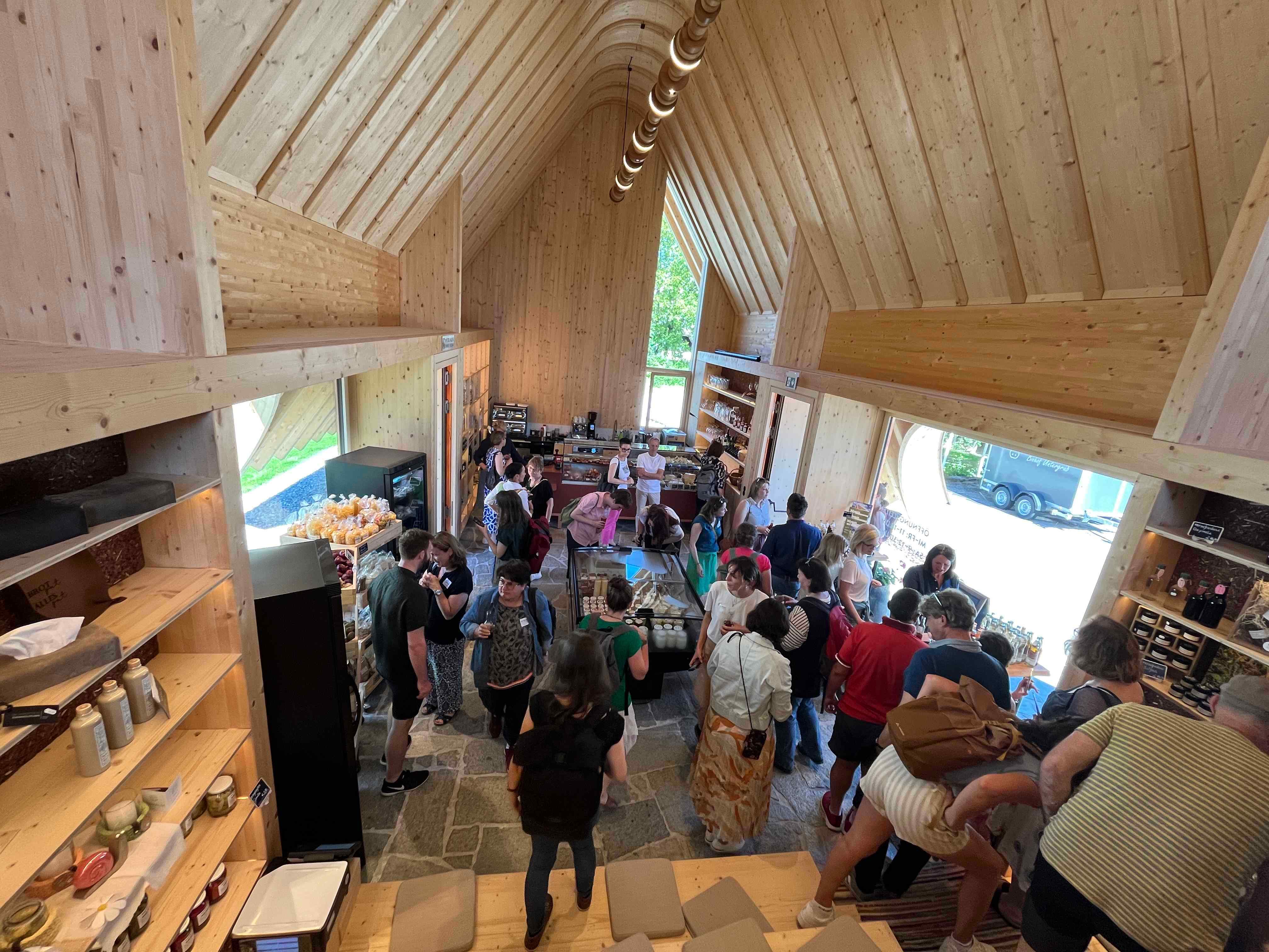 Ein von oben aufgenommenes Bild eines Dorfladens. Es sind viele Menschen im modernen Laden und kaufen ein. 