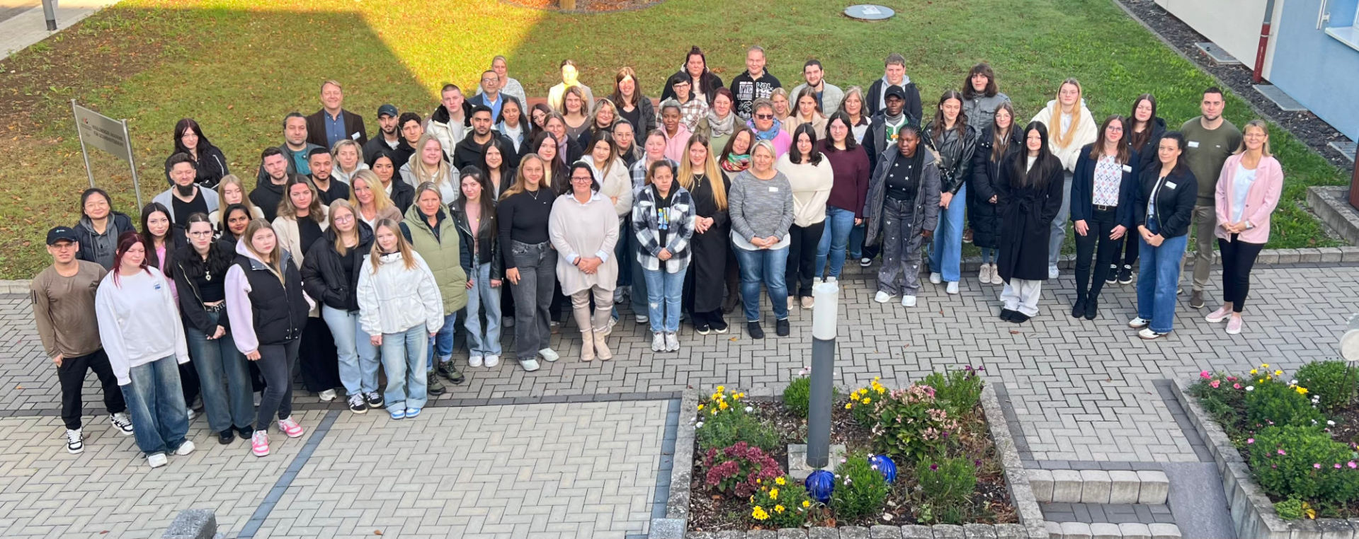 Viele Personen stehen in einem HAlbkreis und schauen nach oben in die Kamera