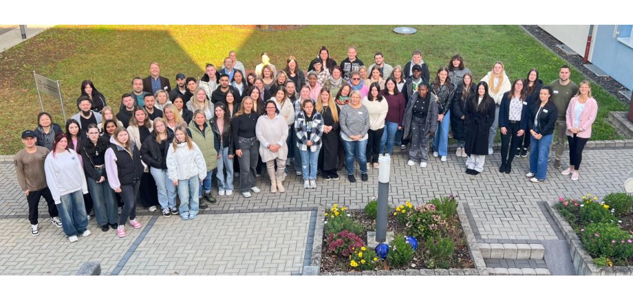 Viele Personen stehen in einem HAlbkreis und schauen nach oben in die Kamera