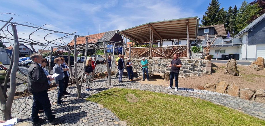 Mehr als 500 Stunden ehrenamtlicher Arbeit der Menschen aus Sichenhausen sind neben Mitteln aus dem Integrierten kommunalen Entwicklungskonzept (IKEK) in die Neugestaltung des Dorfplatzes geflossen. Wo früher das Bauernhaus mit dem Hausnamen „Gritches“ stand, lädt heute ein liebevoll gestalteter Dorfmittelpunkt zum Treffen ein. Ortsvorsteher Martin Grundl (von rechts) und Heinrich Otto Adolph berichten dem Ersten Kreisbeigeordneten Dr. Jens Mischak (Vierter von rechts), Bürgermeisterin Susanne Schaab (Achte von rechts) sowie der Kommission von den Umgestaltungsmaßnahmen. 
