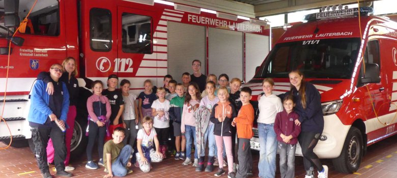 Eine Gruppe Kinder steht vor einem großen Feuerwehrauto. 