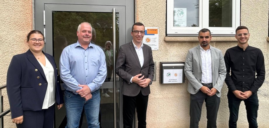 fünf Menschen haben sich für ein Gruppenfoto aufgestellt und lächeln in die Kamera.