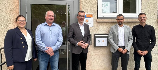 fünf Menschen haben sich für ein Gruppenfoto aufgestellt und lächeln in die Kamera.