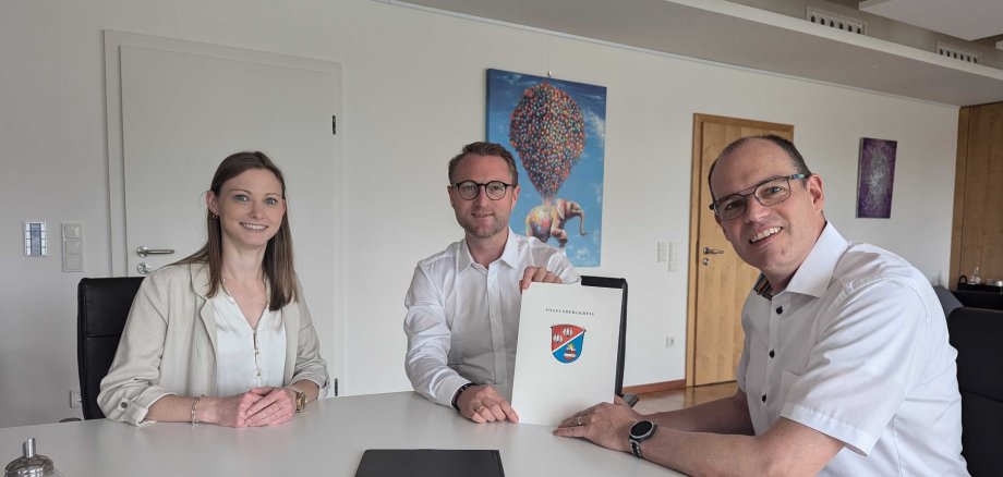 Landrat Dr. Jens Mischak (Mitte) übergibt gemeinsam mit Jana Brittner, vom Amt für Wirtschaft und den ländlichen Raum des Vogelsbergkreises, drei Dorfentwicklungs-Förderbescheide an Sascha Spielberger, Bürgermeister der Gemeinde Freiensteinau. Sie sitzen an einem Tisch und präsentieren die Bescheide