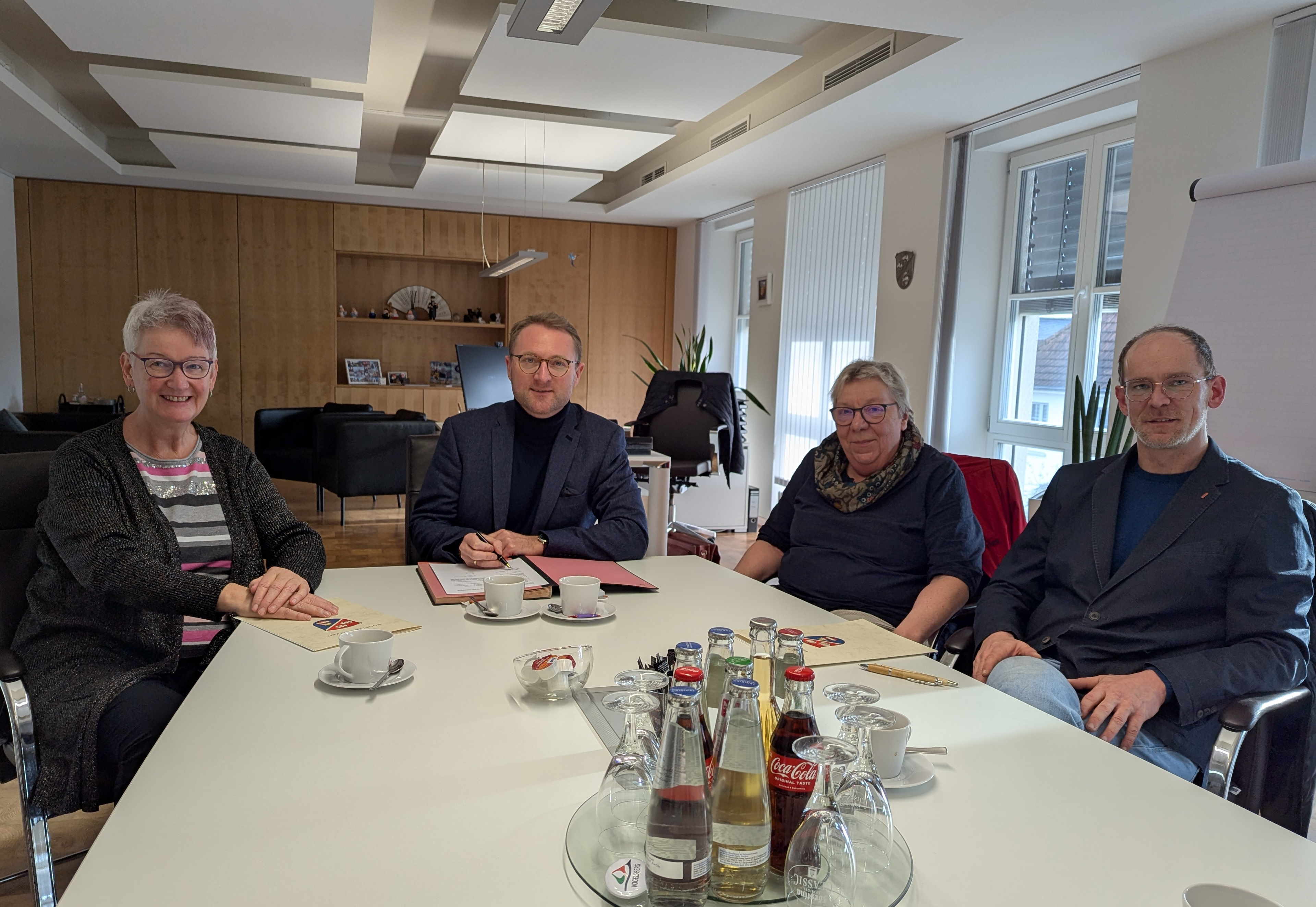 Vier Menschen sitzen an einem Konferenztisch und schauen in die Kamera. Sie haben gerade einen Vertrag unterzeichnet, der die Sozialarbeit in Schulen im Vogelsbergkreis regelt. 