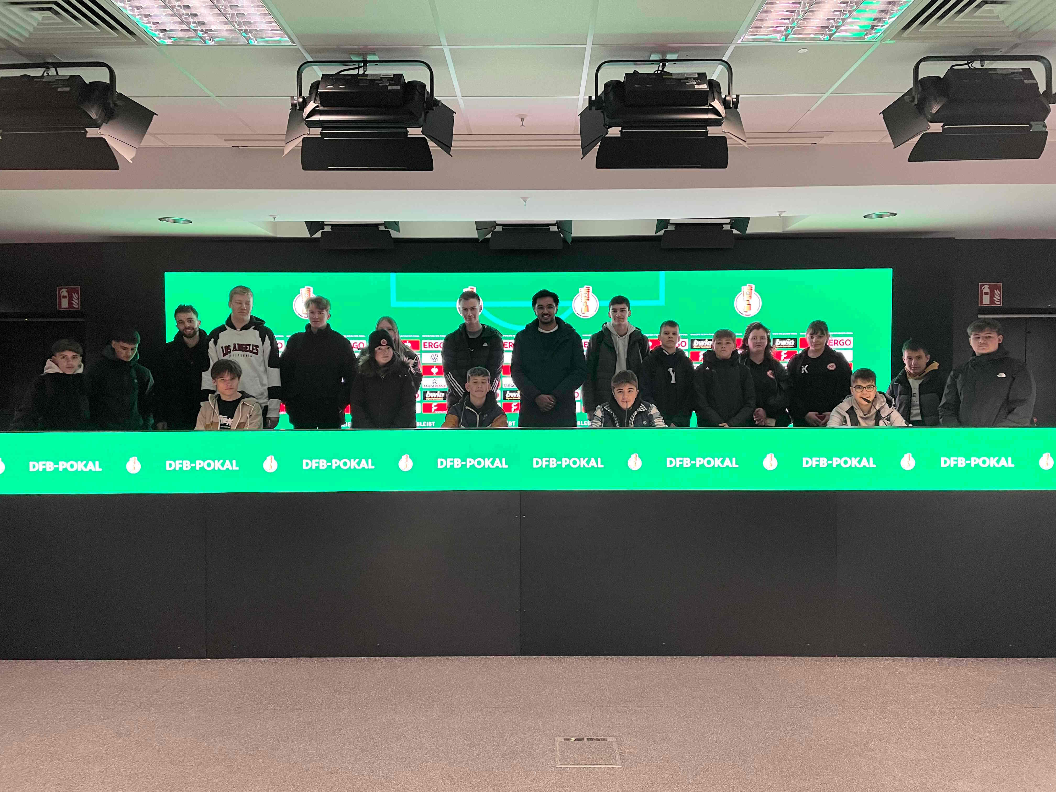 Eine Gruppe Jugendlicher steht im Stadion der Frankfurter Eintracht dort, wo sonst Spieler und Trainer bei Pressekonferenzen sitzen