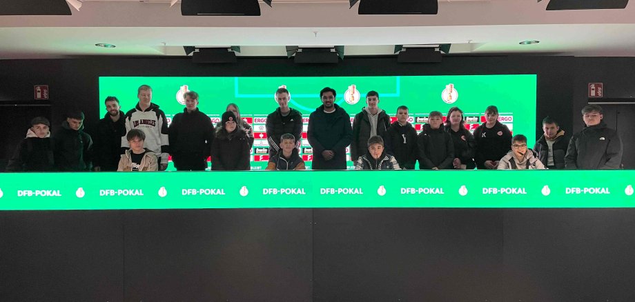 Eine Gruppe Jugendlicher steht im Stadion der Frankfurter Eintracht dort, wo sonst Spieler und Trainer bei Pressekonferenzen sitzen