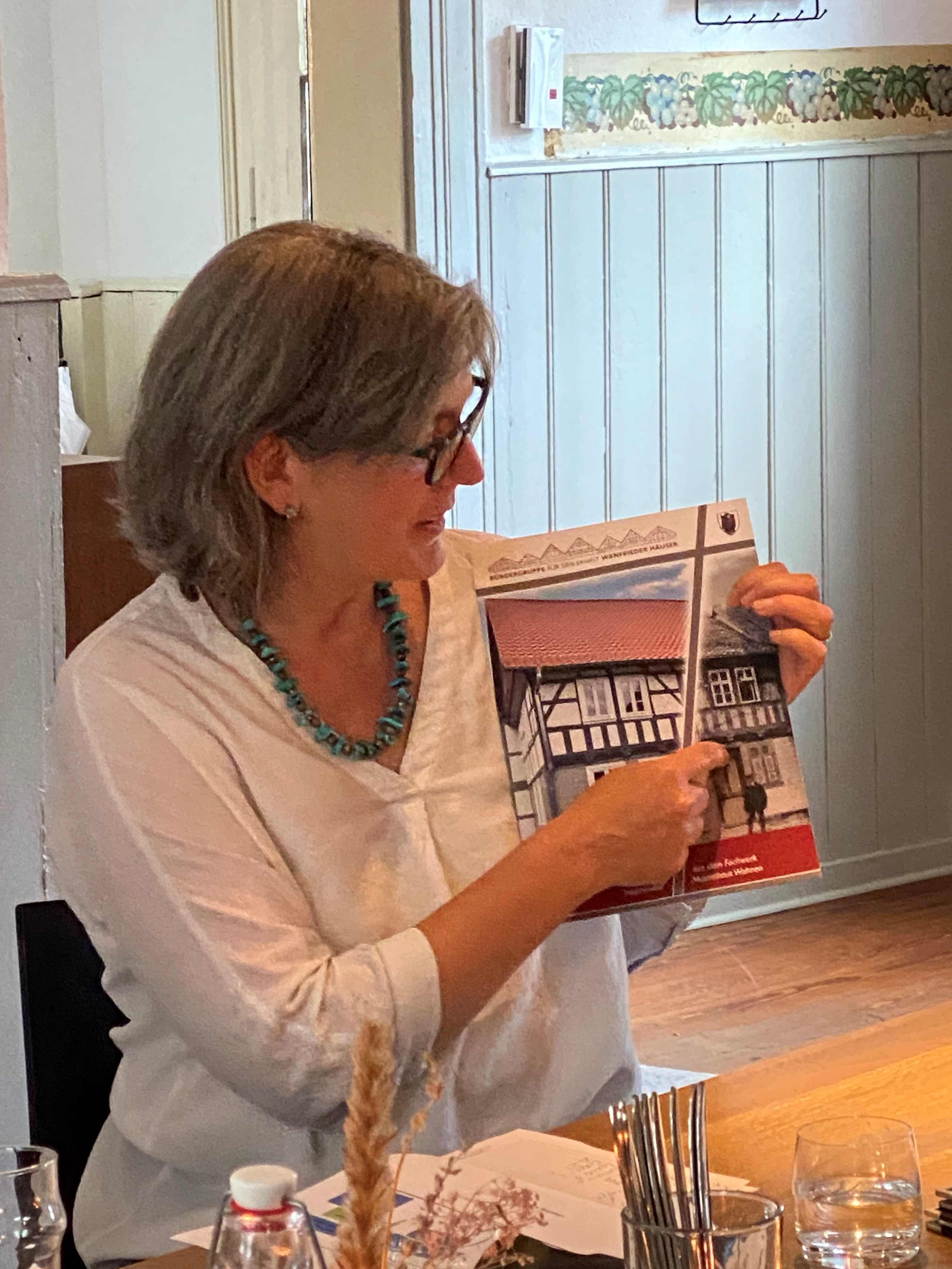 Referentin Diana Wetzestein zeigt auf einer Broschüre auf ein Bild eines alten Fachwerkhauses.
