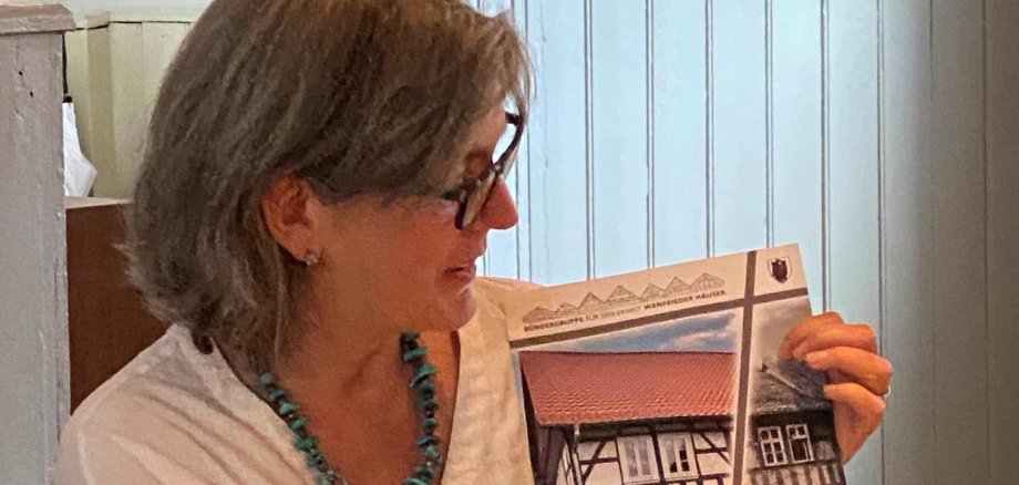 Referentin Diana Wetzestein zeigt auf einer Broschüre auf ein Bild eines alten Fachwerkhauses.