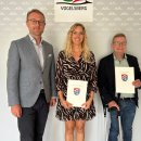 Drei Menschen haben sich vor eine graue Wand zum Gruppenfoto aufgestellt. Es sind zwei Männer und eine Frau zu sehen, die in die Kamera lächeln.