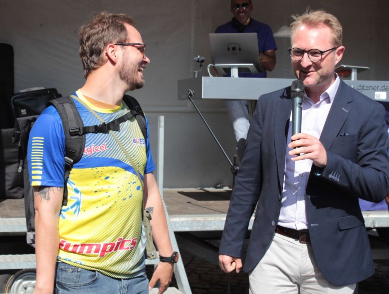 Bewegungskoordinator Dominic Günther und Dr. Jens Mischak vor einer Bühne. Sie sprechen zu den Gästen