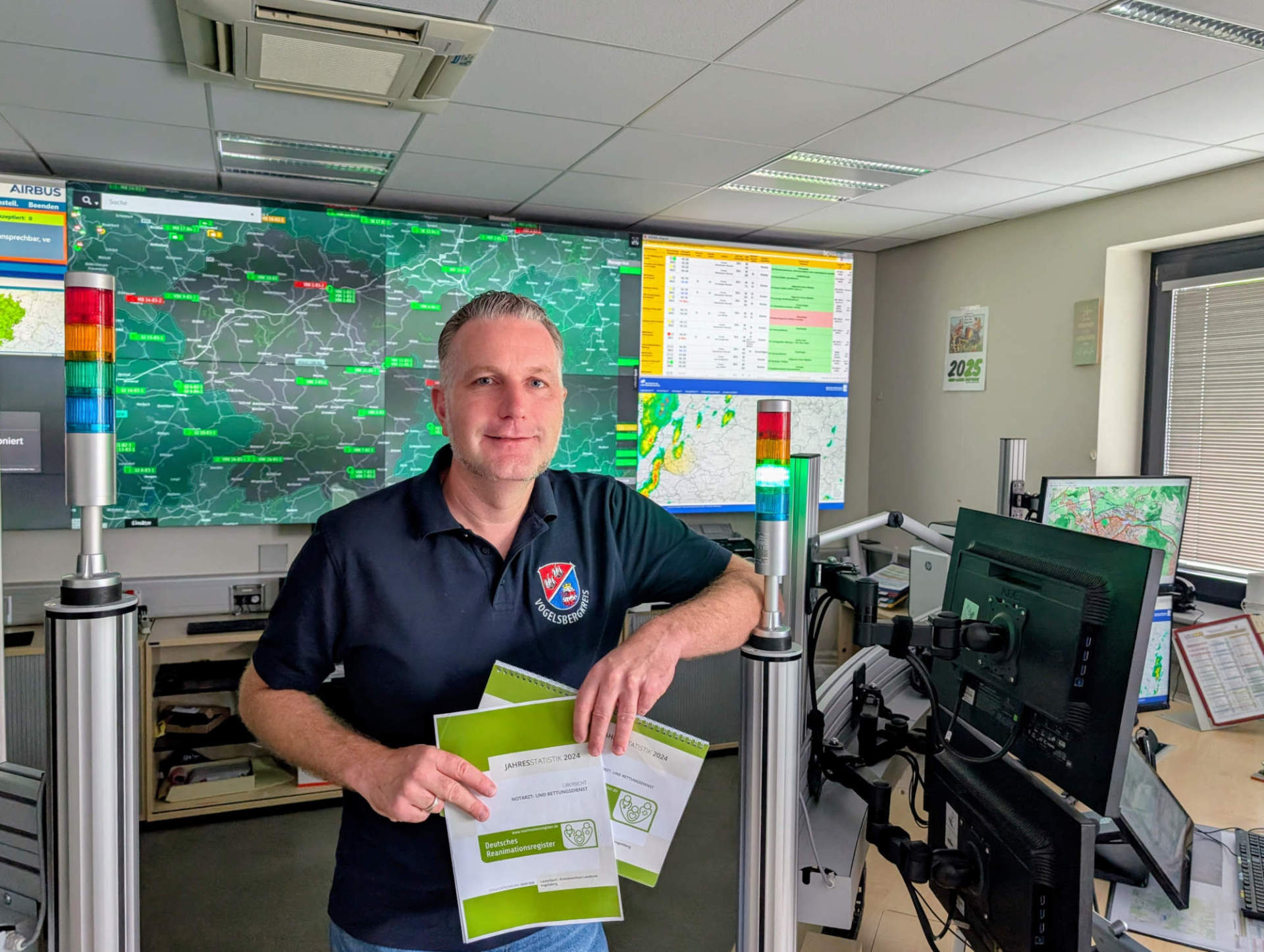 Dr. Dennis Humburg, ärztlicher Leiter des Rettungsdiensts im Vogelsbergkreis, präsentiert die Daten des Reanimations-Register für den Vogelsbergkreis. Er steht vor einer Videowand, an der Rettungsdienstinformationen und KArten zu sehen sind.