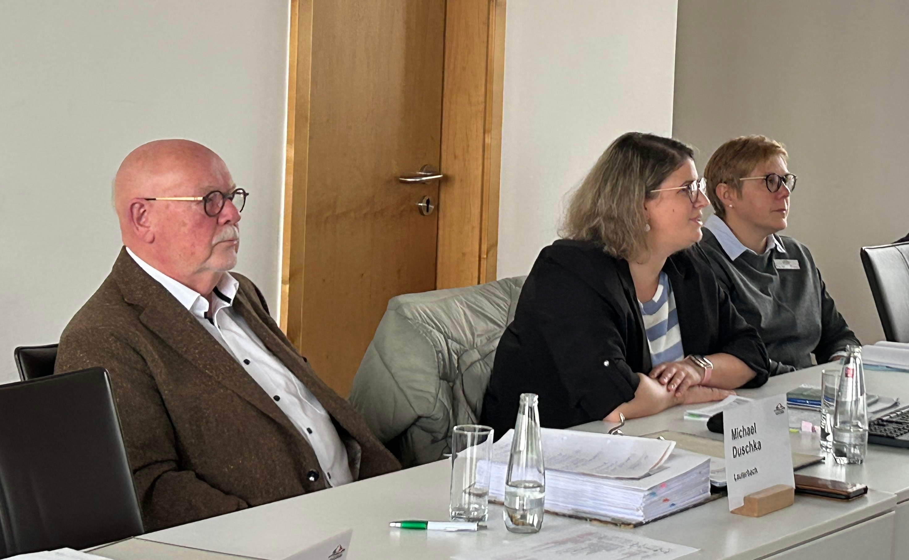 Ein Mann und zwei Frauen sitzen vor einem Plenum und sprechen mit den Anwesenden. 