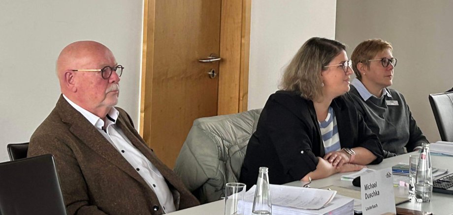 Ein Mann und zwei Frauen sitzen vor einem Plenum und sprechen mit den Anwesenden. 