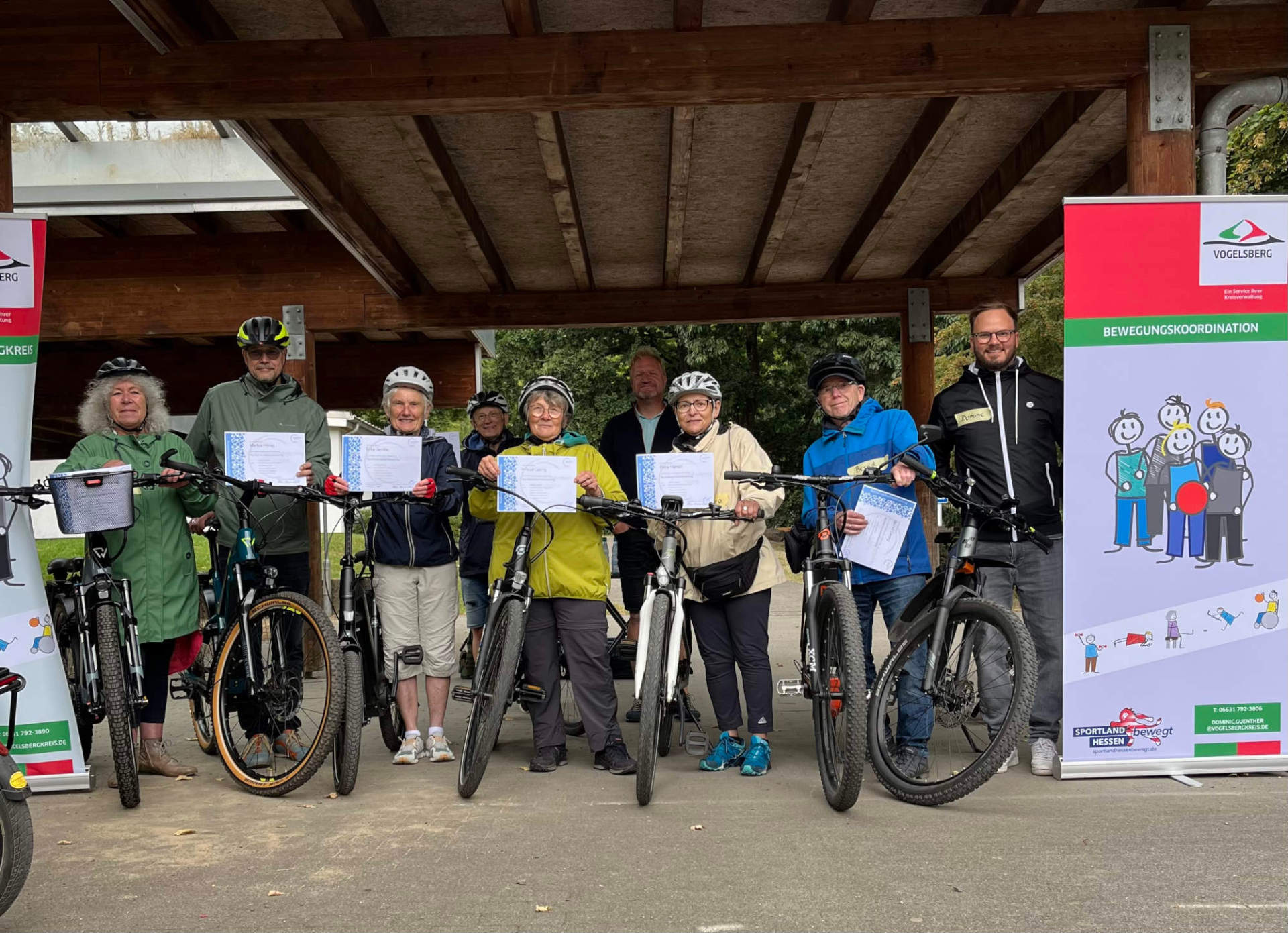 Mehrere Menschen lächeln in die Kamera. Sie sind in Radklamotten gekleidet und stehen neben ihren Fahrrädern