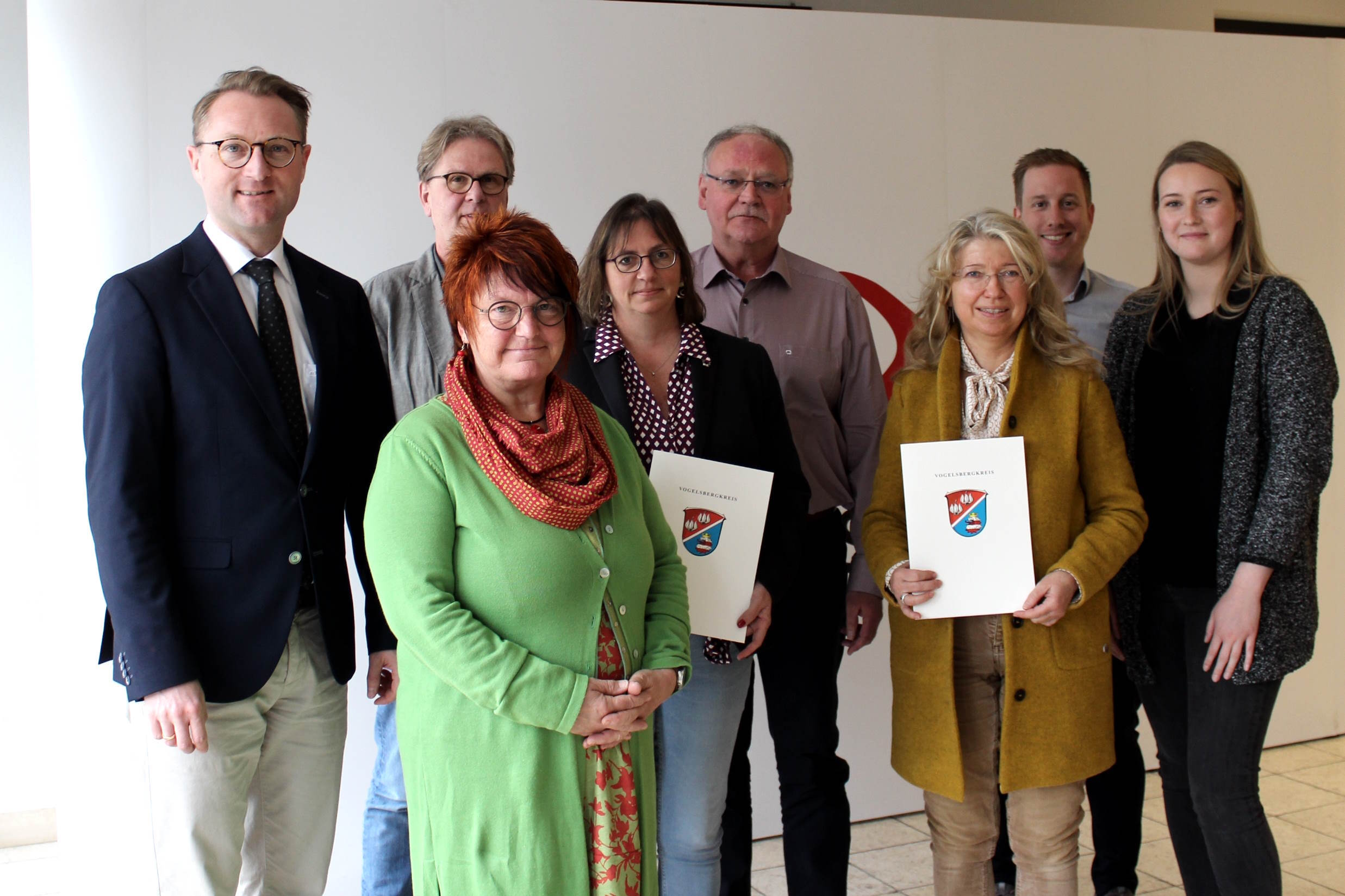 Eine Gruppe von Menschen steht vor einer weißen Fotowand. 