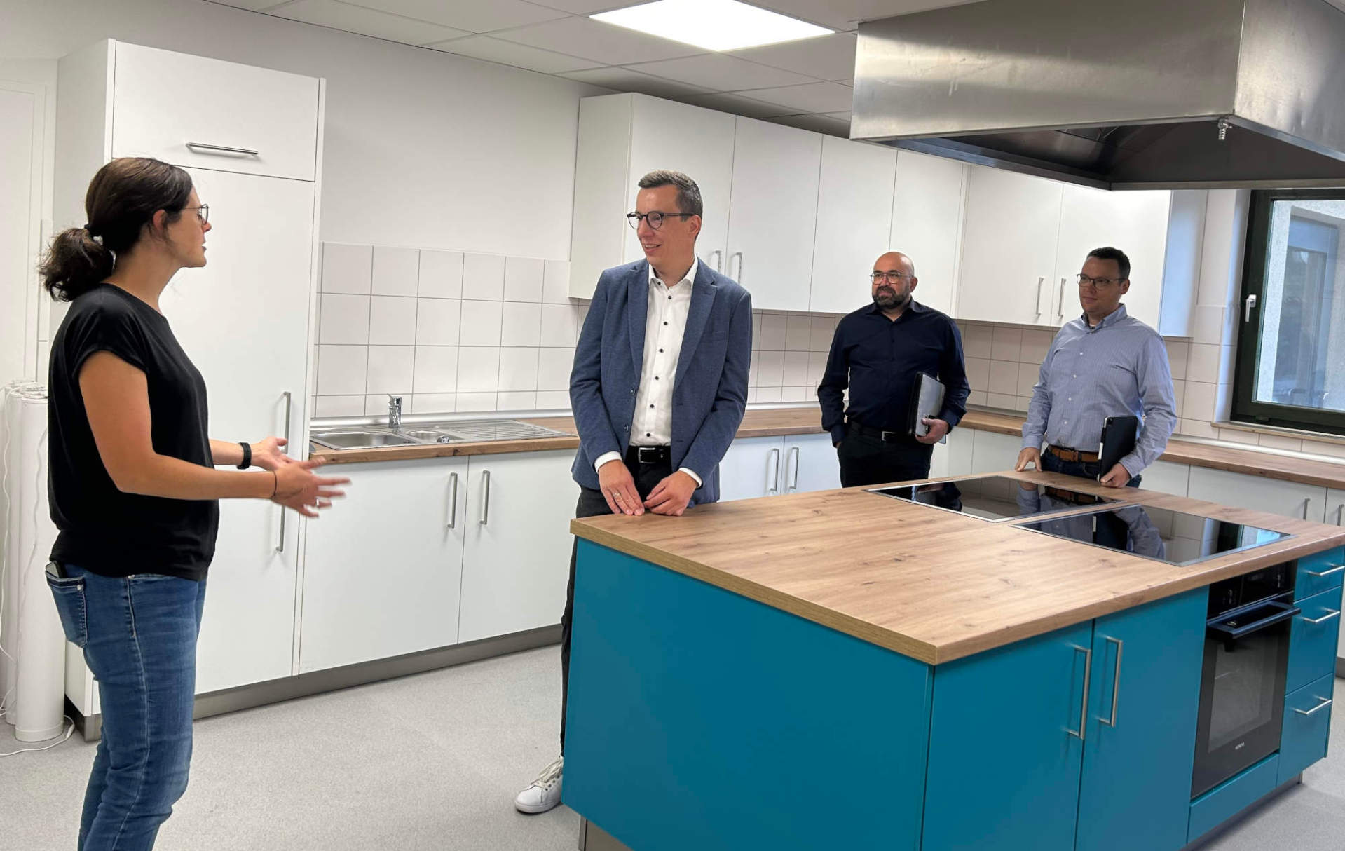 Eine Frau und drei Männer stehen in einer neuen Schulküche und sprechen darüber.