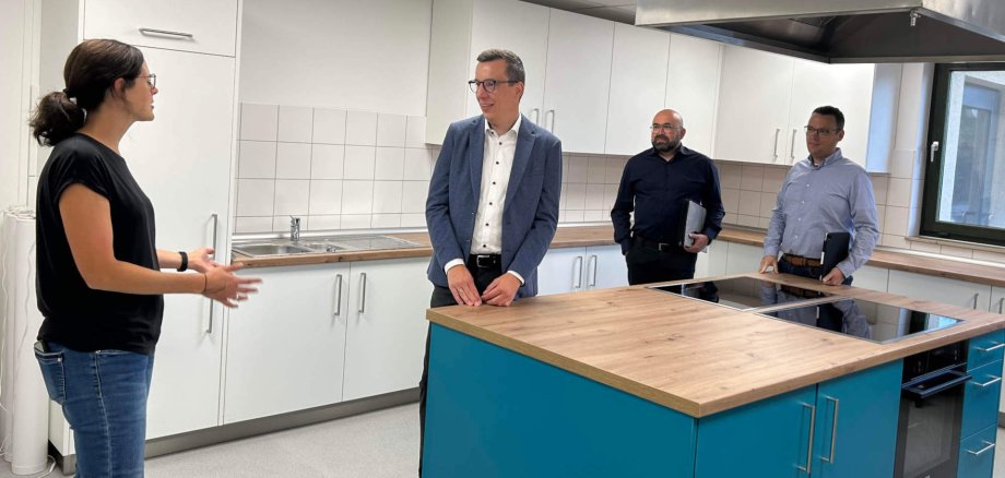 Eine Frau und drei Männer stehen in einer neuen Schulküche und sprechen darüber.