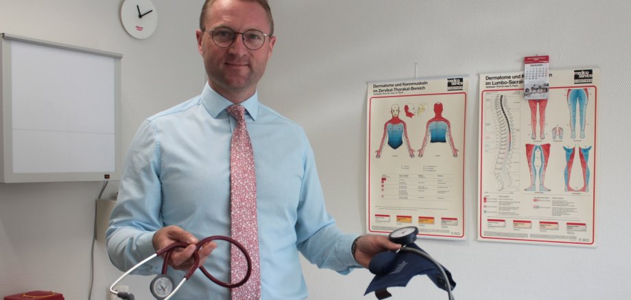 Dr. Jens Mischak hält ein Stethoskop und eine Blutdruckmessmanschette in die Kamera