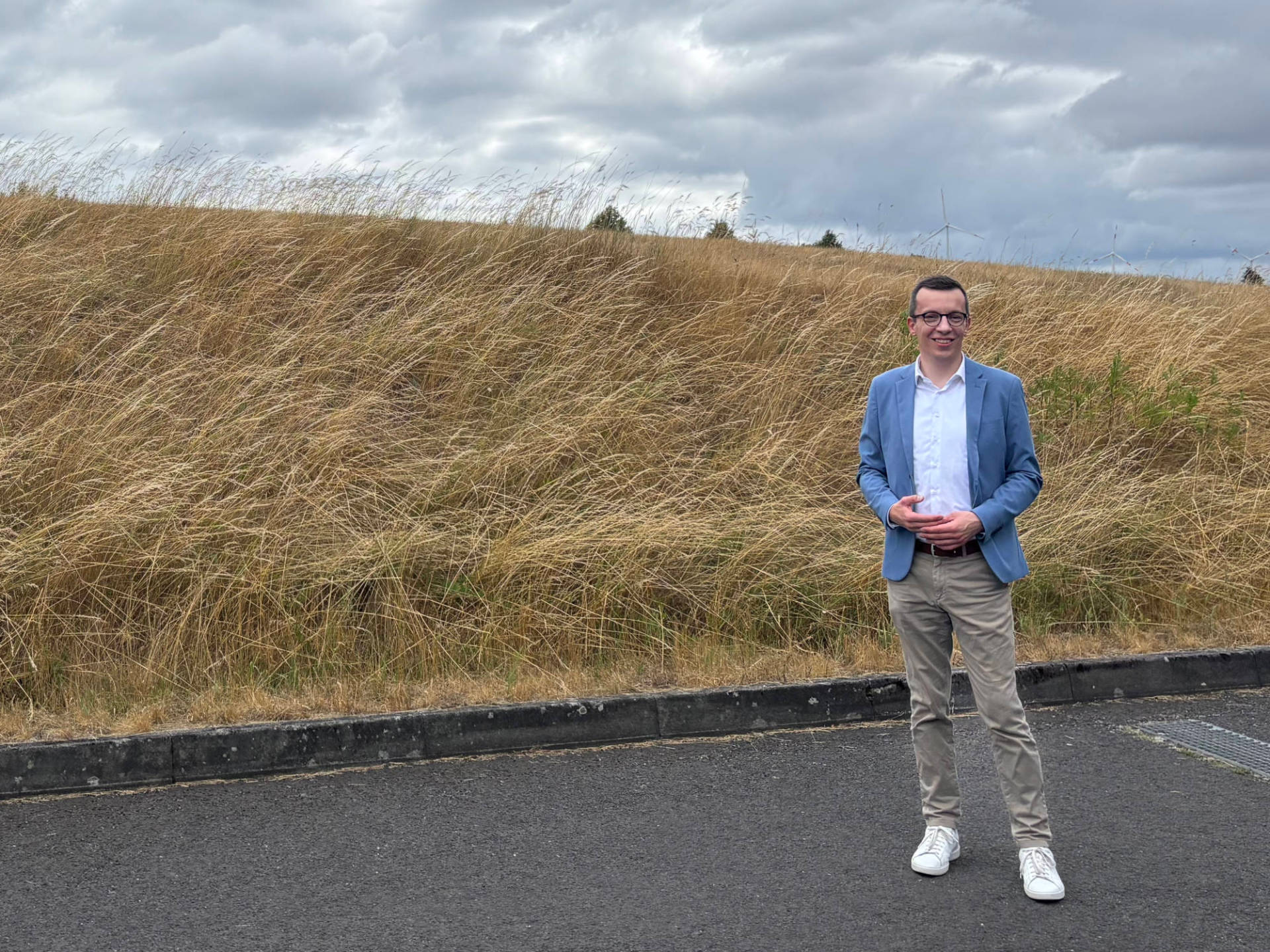 Auf dem Grundstück im Hintergrund sollen die Bauarbeiten für die neue Grundschule im kommenden Jahr starten: Erster Kreisbeigeordneter und Schuldezernent am Ende der Jahnstraße in Brauerschwend, oberhalb von Sporthalle und Cornelia-Funke-Schule. Patrick Krug steht auf einer Straße vor einer Wiese.