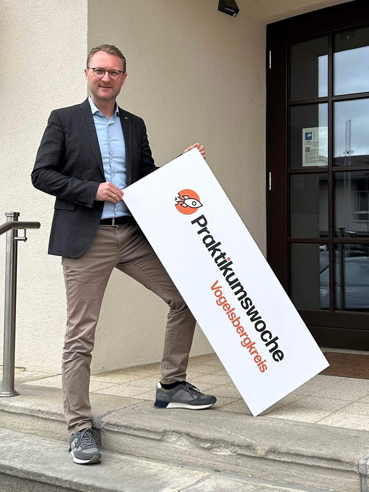 Dr. Mischak hält ein Schild in die Kamera. Darauf wird für die Praktukumswochen im Vogelsbergkreis geworben.