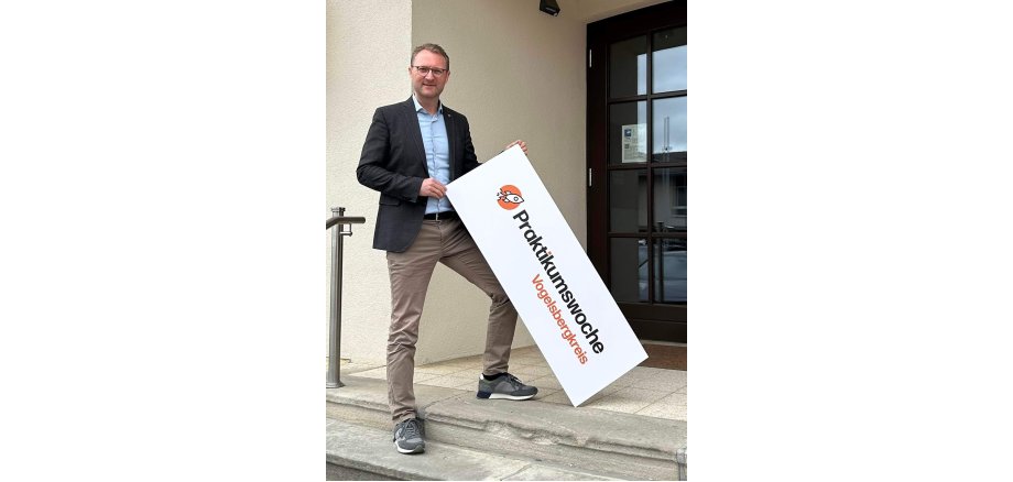 Dr. Mischak hält ein Schild in die Kamera. Darauf wird für die Praktukumswochen im Vogelsbergkreis geworben.