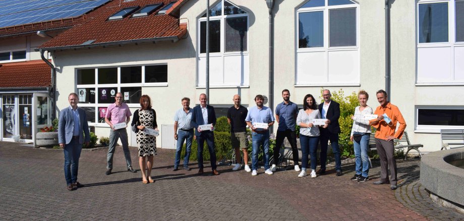 Der Erste Kreisbeigeordnete Dr. Jens Mischak (links, CDU) überreicht gemeinsam mit Thomas Schaumberg (Vierter von links), vom Verein Region Vogelsberg, und Edwin Schneider (Fünfter von links), LEADER-Beiratsvorsitzender und Bürgermeister der Stadt Ulrichstein, die Förderplaketten. Sascha Spielberger (von links), Bürgermeister der Gemeinde Freiensteinau, Doris Wirkner, Evangelische Dekanate Grünberg, Hungen und Kirchberg, André Metz vom Zeltlagerverein, Jörg Reichel, Erster Vorsitzender des Zeltlagervereins Eckmannshain, Jan Philip Christof, Zweiter Vorsitzender des Zeltlagervereins Eckmannshain, Daniela Bauernfeind, Inklusionsbeauftragte, Vorstandsmitglied und Projektverantwortliche des Schützenvereins Nieder-Ohmen, Markus Enders, Erster Vorsitzender des Schützenvereins Nieder-Ohmen, Doro Bork, Vorstandsmitglied des Vereins Über-Brücken/over-bridges, und Frank Händeler, künstlerischer Leiter und Vorsitzender des Vereins Über-Brücken/over-bridges nehmen die Förderung dankend entgegen. 