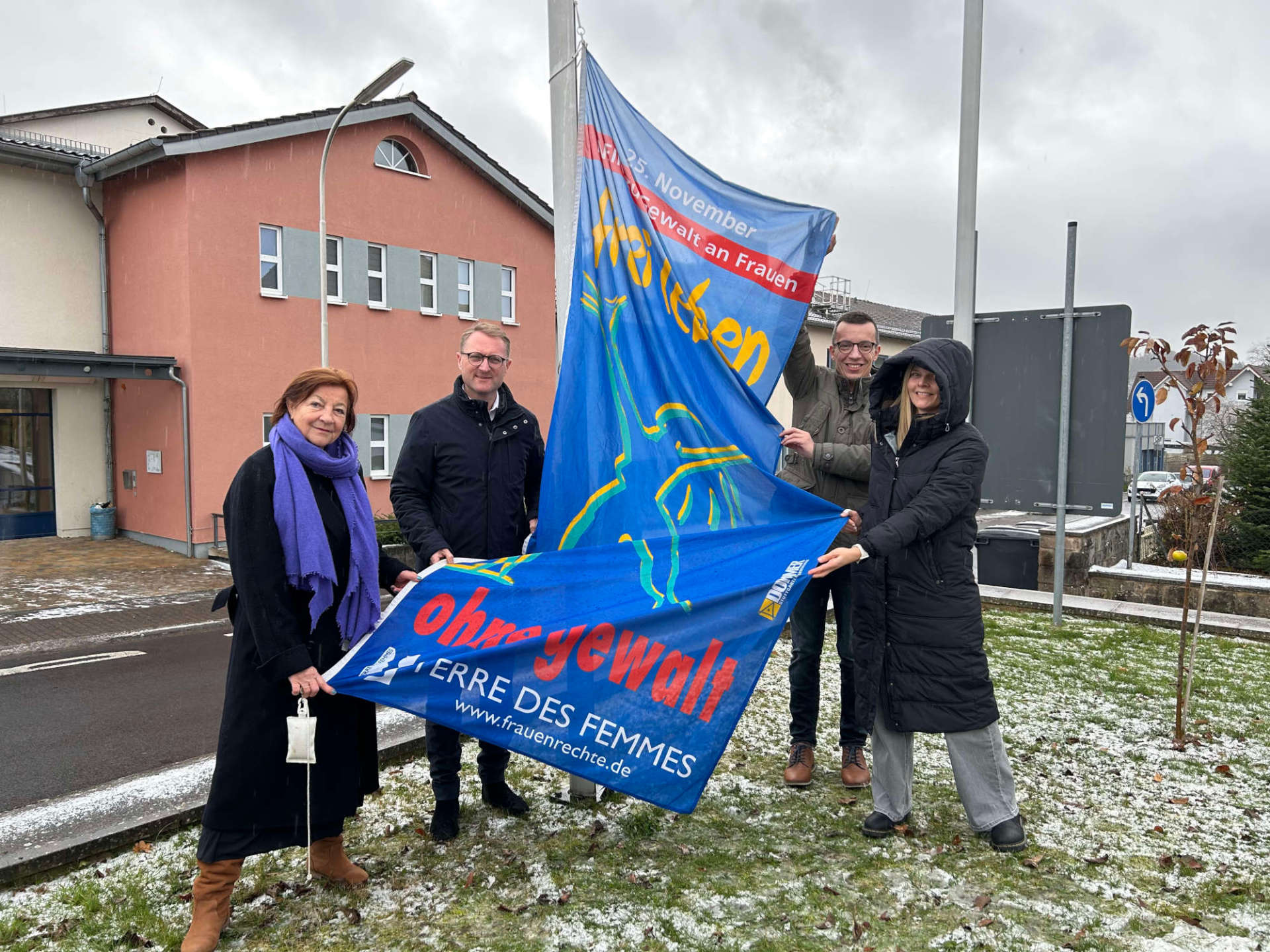 Vier Personen hissen symbolisch eine Flagge, die zum Schutz von Frauen gegen Gewalt aufruft. 