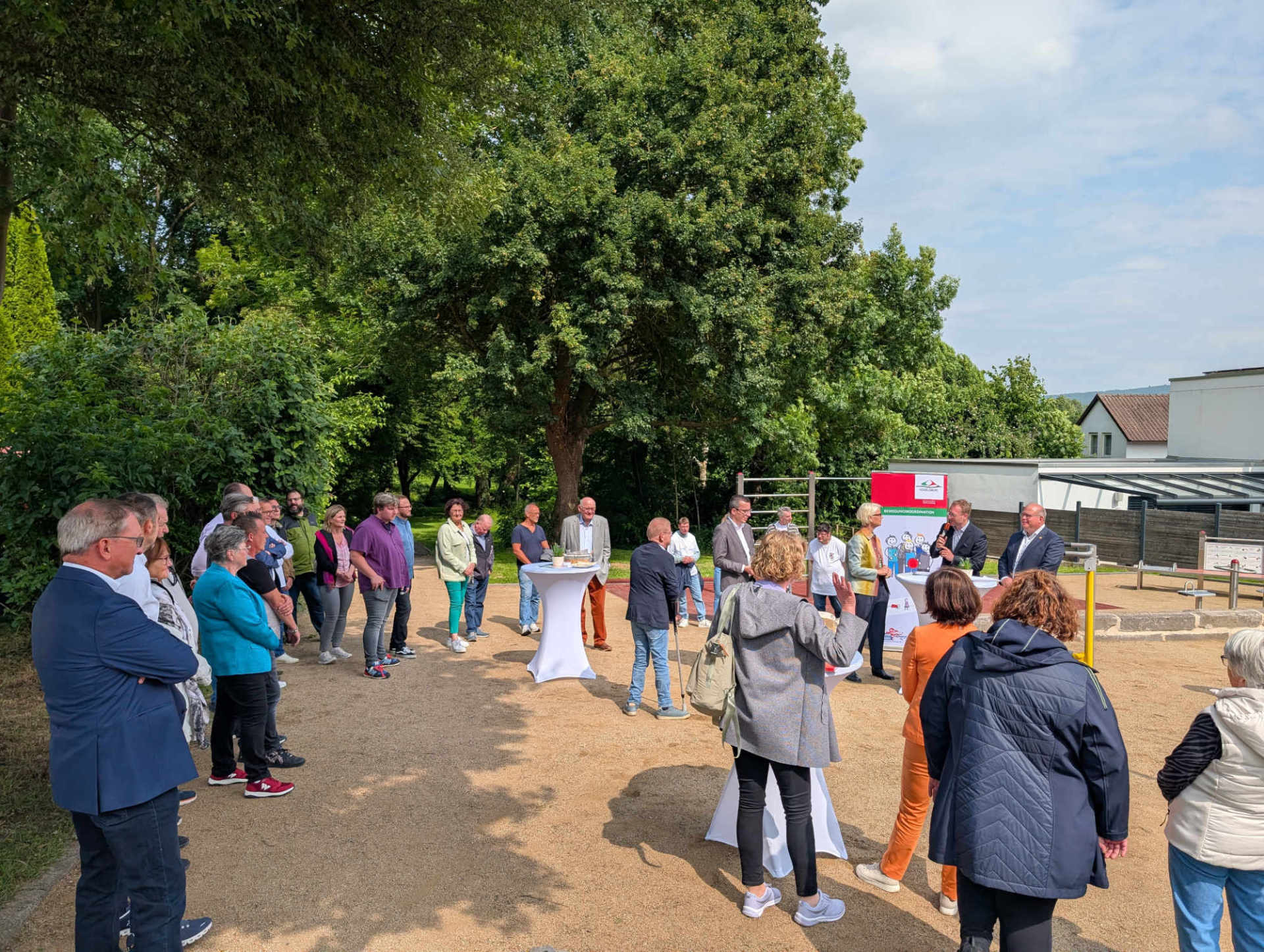 Viele Menschen stehen rund um  einen inklusiven Bewegungspark mit verschiedenen Sportgeräten. Dieser wird gerade feierlich eröffnet