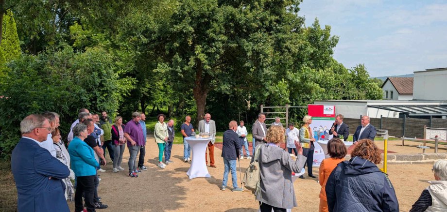 Viele Menschen stehen rund um  einen inklusiven Bewegungspark mit verschiedenen Sportgeräten. Dieser wird gerade feierlich eröffnet
