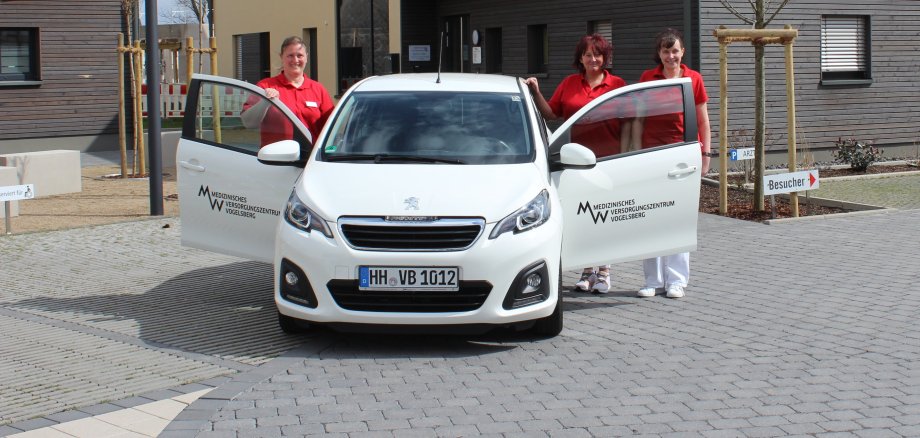 Als verlängerter Arm des Ärzteteams unterwegs: Julia Förster (von links), Sabrina Deuchert, und Meike Schauermann bringen langjährige Erfahrungen als Medizinische Fachangestellte mit und entlasten die Ärzte des MVZ Vogelsberg. Sie stehen an einem weißen Auto vor dem MVZ-Gebäude
