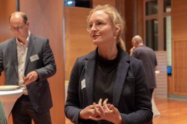 Im Vordergrund ist eine Frau im Gespräch zu erkennen. Im Hintergrund steht ein Mann an einem Stehtisch.