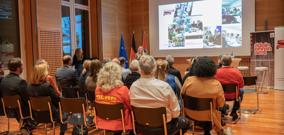 Rund 50 Personen sitzen in einem Veranstaltungsraum und hören einem Vortrag zu