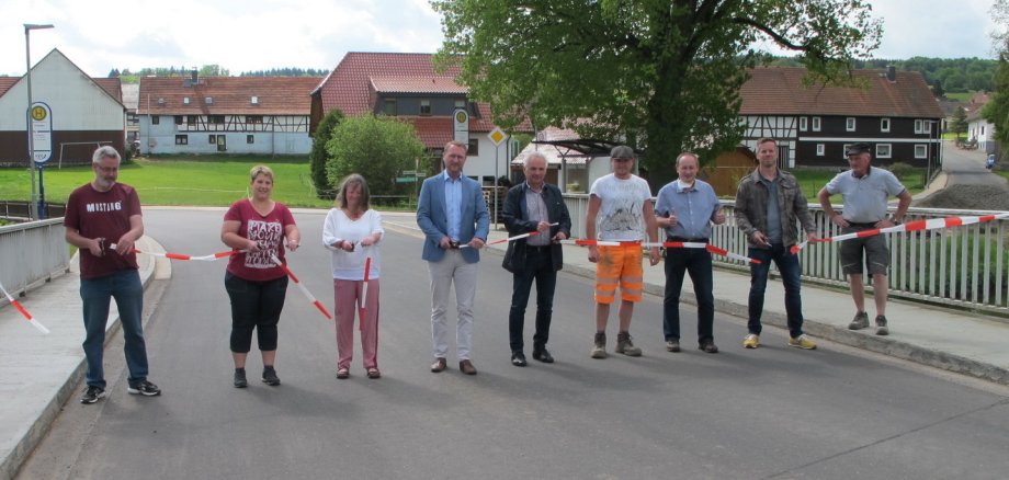 Gaben gemeinsam die Ortsdurchfahrt offiziell für den Verkehr frei: Dr. Jens Mischak (Vierter von links), Erster Kreisbeigeordneter, gemeinsam mit Sebastian Stang (Dritter von rechts), Bürgermeister der Gemeinde Grebenhain, Günter Herles  (Fünfter von rechts), Hessen Mobil, Stefan Günther (Zweiter von rechts), Sachgebietsleiter Kreisstraßen im Amt für Bauen und Umwelt, durchtrennen gemeinsam mit weiteren Vertreterinnen und Vertretern das Band. 
