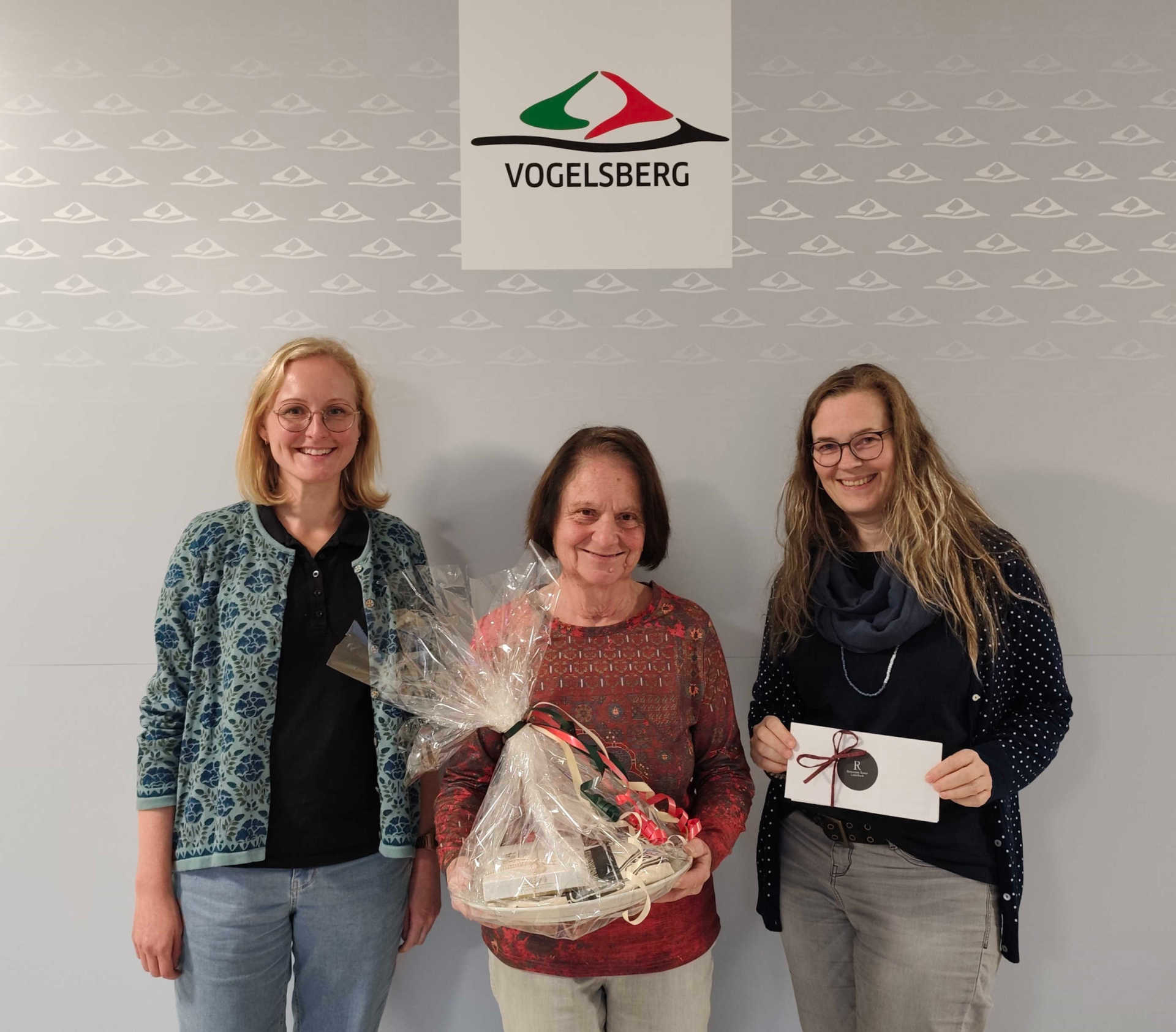 Drei Frauen lächeln in die Kamera. eine hält ein kleines Geschenk in der Hand