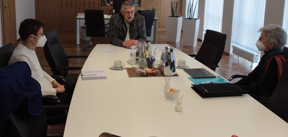 Prof. Dr. Helma Blese (rechts) stellt ihr neues Forschungsprojekt FreiZeit im Gespräch mit Landrat Manfred Görig und Dr. Sigrid Stahl, Leiterin der Fachstelle Gesundheitliche Versorgung beim Vogelsbergkreis, vor.  Sie sitzen an einem weißen Tisch in einem Büro.