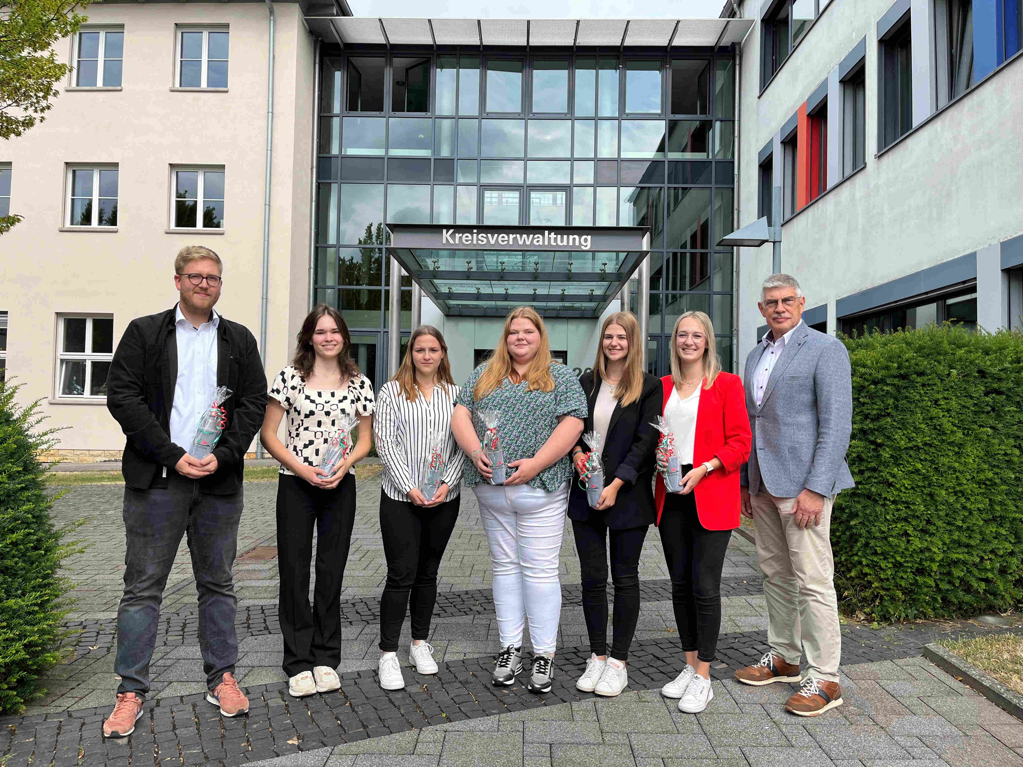 Geschafft! Landrat Manfred Görig gratuliert Marie Vaupel, Annika Goll, Sarah Kuhla, Cora Weiß, Alina Warkentin und Patrick Döring (von rechts) zu ihren Super-Ergebnissen bei den Abschlussprüfungen. Sie haben sich zum Gruppenbild vor dem Haupteingang der Kreisverwaltung aufgestellt.
