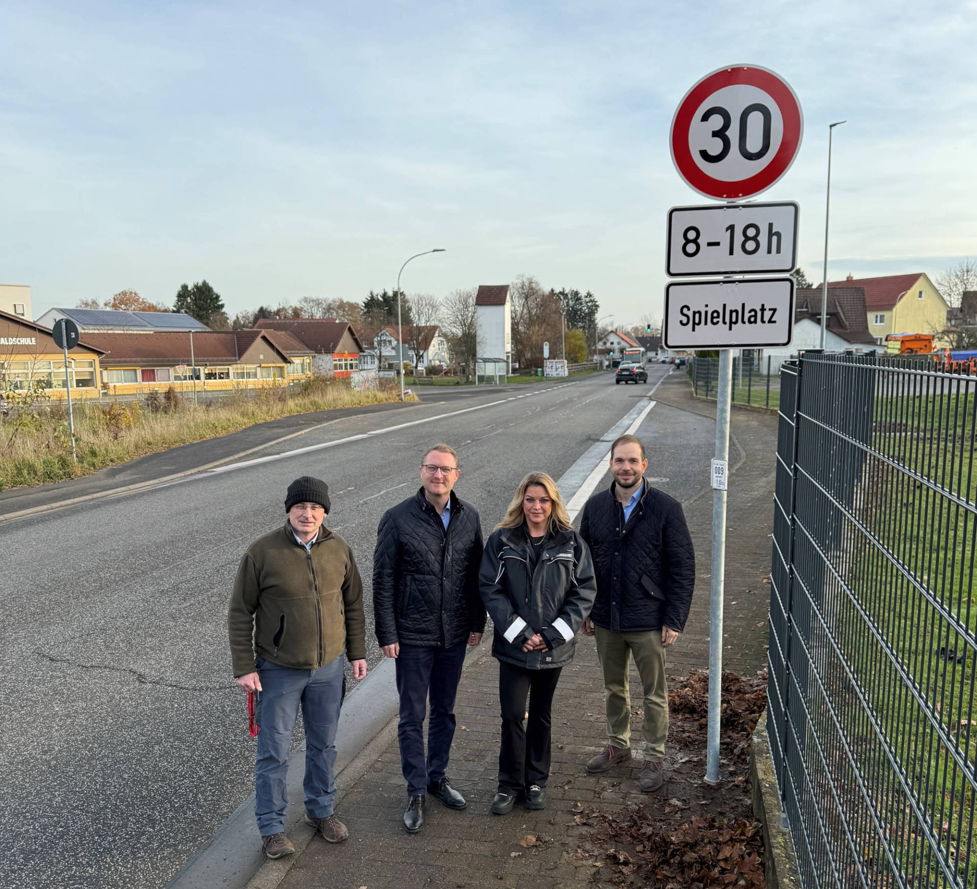 Vier Menschen stehen an einer STraße und präsentieren ein Verkehrsschild.
