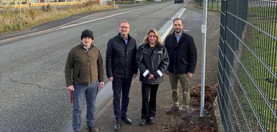 Vier Menschen stehen an einer STraße und präsentieren ein Verkehrsschild.