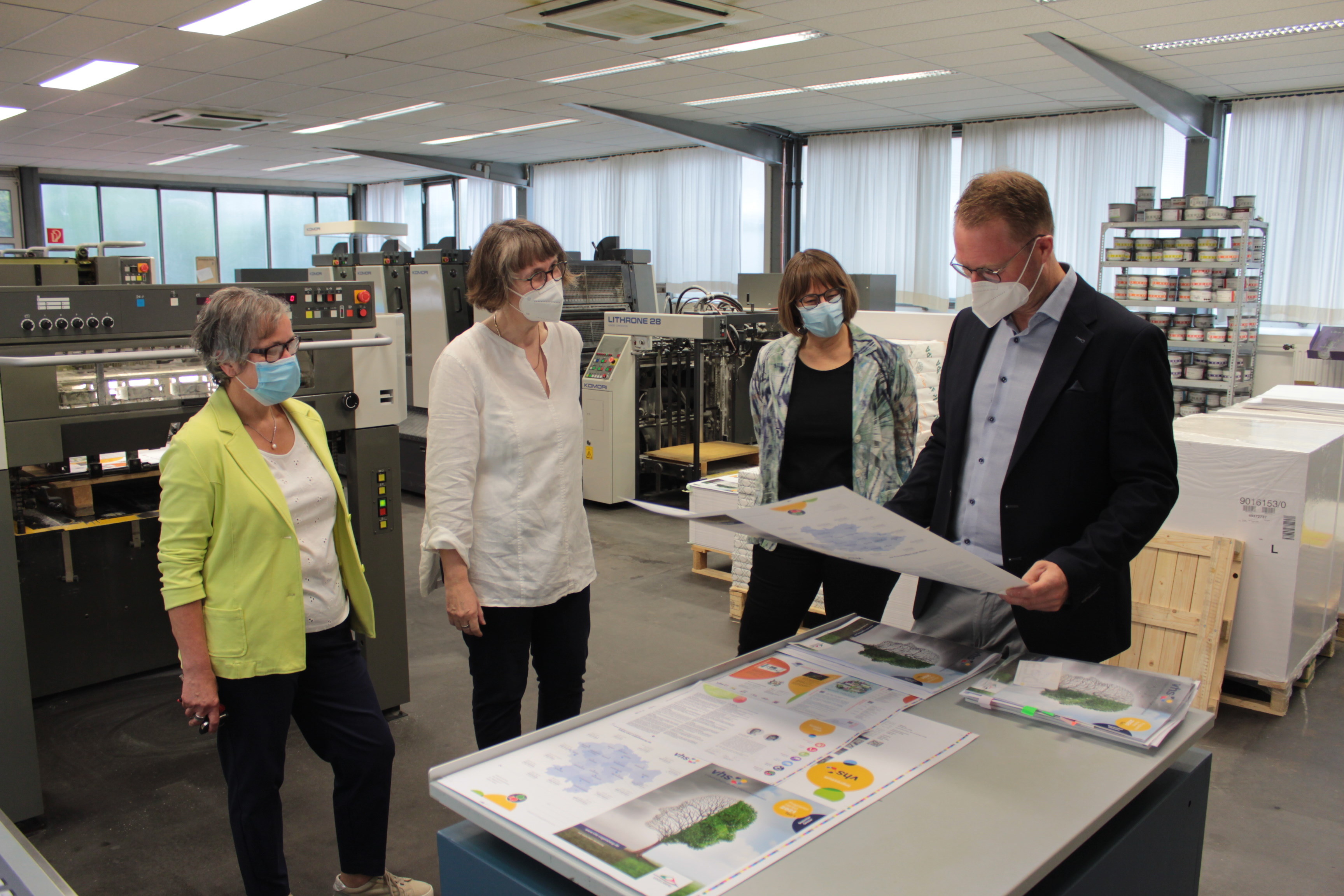Der Erste Kreisbeigeordnete Dr. Jens Mischak (CDU, rechts), wirft gemeinsam mit Monika Schenker (von rechts), Leiterin des Amtes für Volkshochschule, Petra Dörr-Eisenträger, von der Lauterbacher Druckerei Mergard, und Karin Gröger, stellvertretende Amtsleiterin und Fachbereichsleitung Gesundheit und Gesellschaft einen Blick auf die Konzeption und erste Druckbögen.