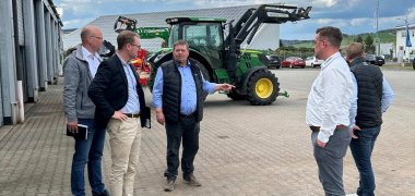 Fünf Personen stehen auf dem Hof einer Landmaschinenwerkstatt vor einem Traktor.