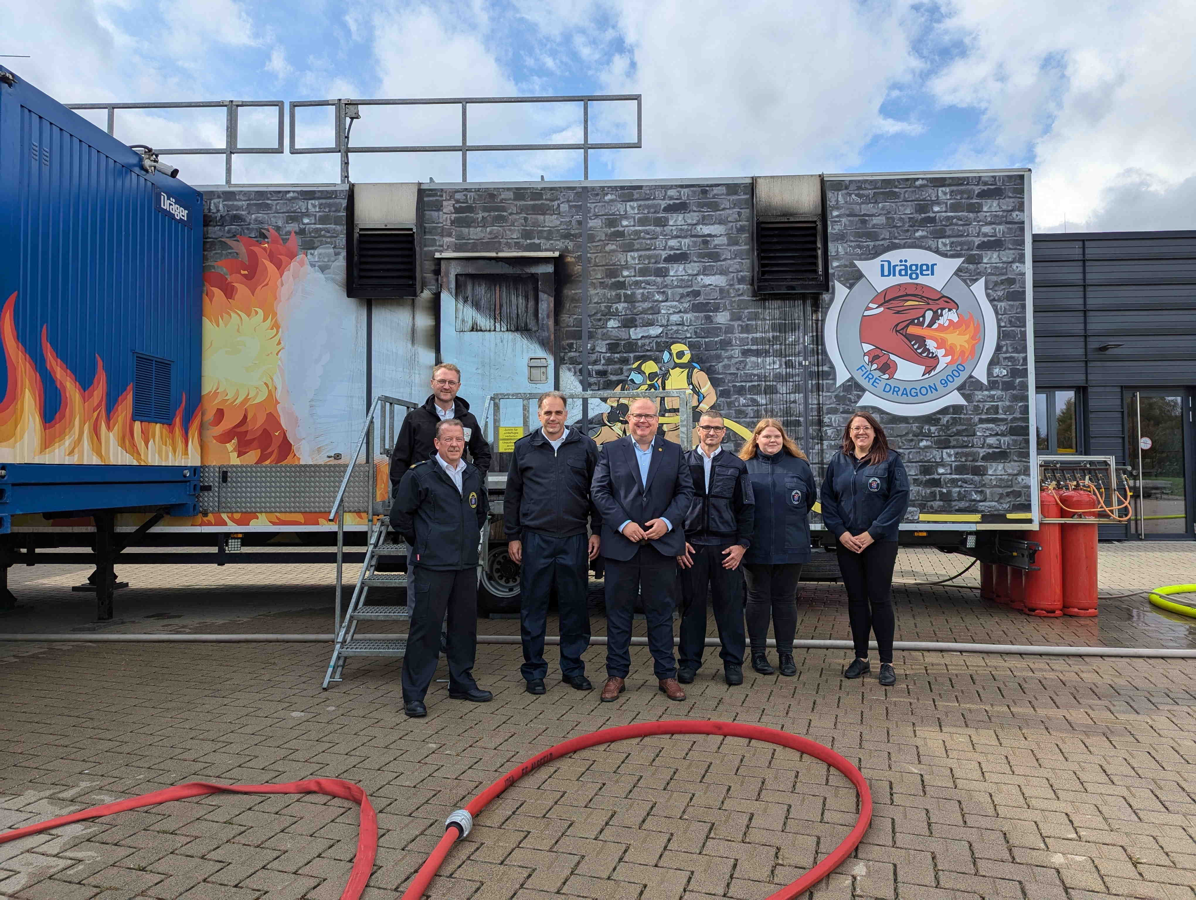 Sieben Personen haben sich vor einer Brandsimulationsanlage zum Gruppenbild aufgestellt.