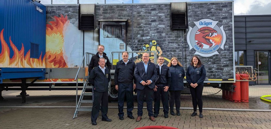 Sieben Personen haben sich vor einer Brandsimulationsanlage zum Gruppenbild aufgestellt.