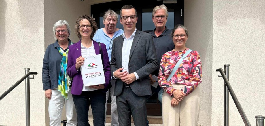 Sechs Personen haben sich auf einer Treppe für ein Gruppenfoto aufgestellt, und lächeln in die Kamera. Darunter sind auch Erster Kreisbeigeordneter Patrick Krug und Kirchenpräsidentin Prof. Dr. Christine Tietz.